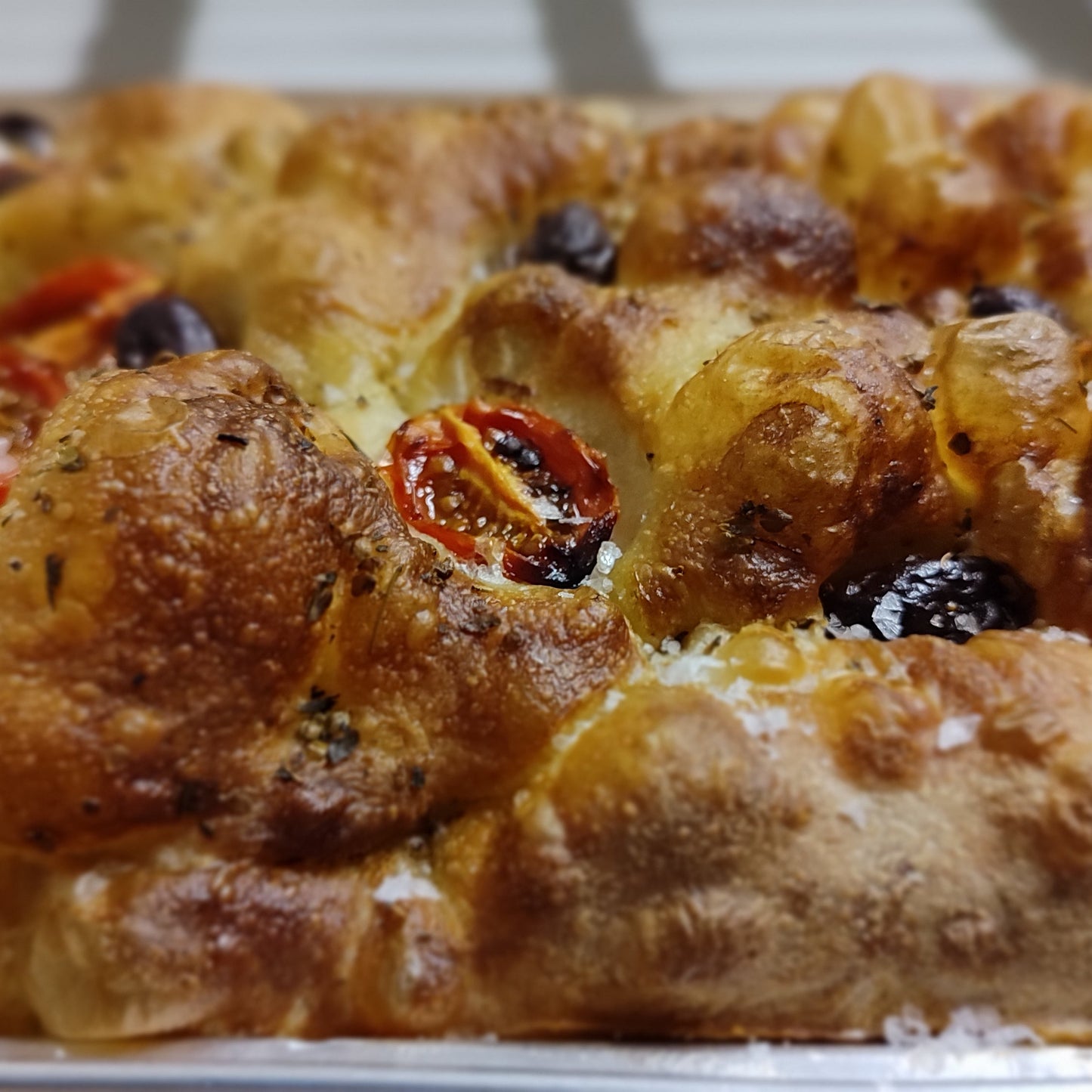 Close-up of a sourdough Focaccia loaf with cherry tomatoes and olives on a white plate