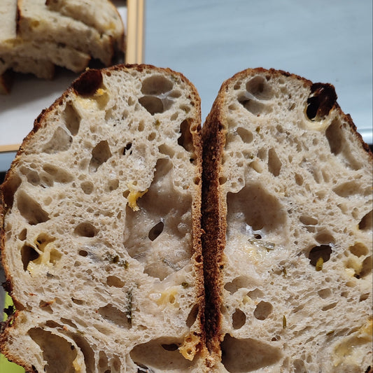 A close-up of a rustic artisan bread loaf sliced open to show the airy crumb structure, held in a hand over a green cutting board with more bread pieces in the background.