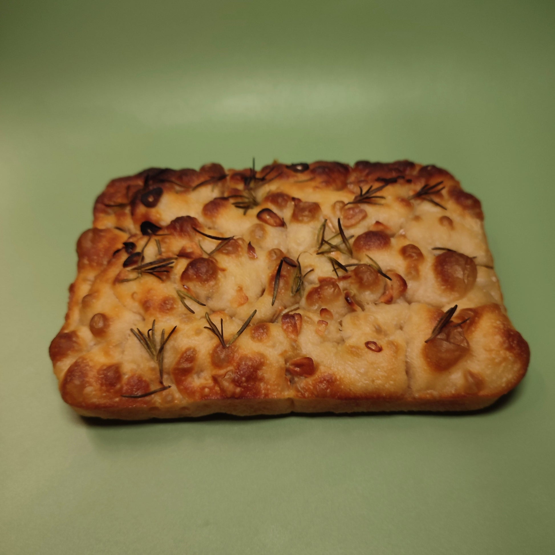 Rectangular focaccia bread with rosemary on a green background