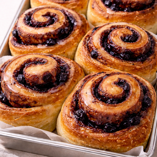 Baked cinnamon rolls with blueberry swirls on a metal tray.